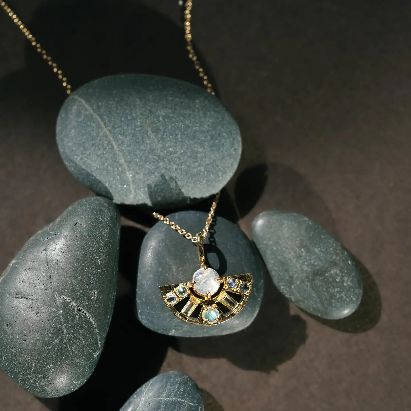 Half circle moonstone and topaz pendant on grey rocks on brown background