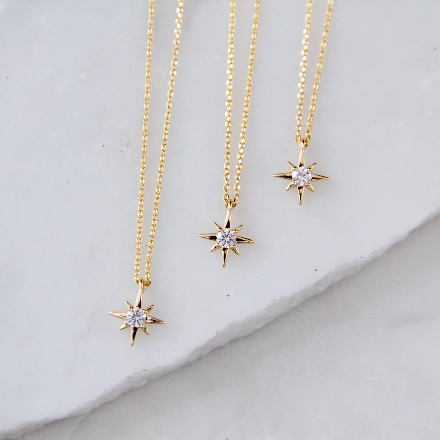 Three gold star-shaped necklaces with diamond-like stones on a light gray surface.