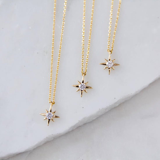 Three gold star-shaped necklaces with diamond-like stones on a light gray surface.