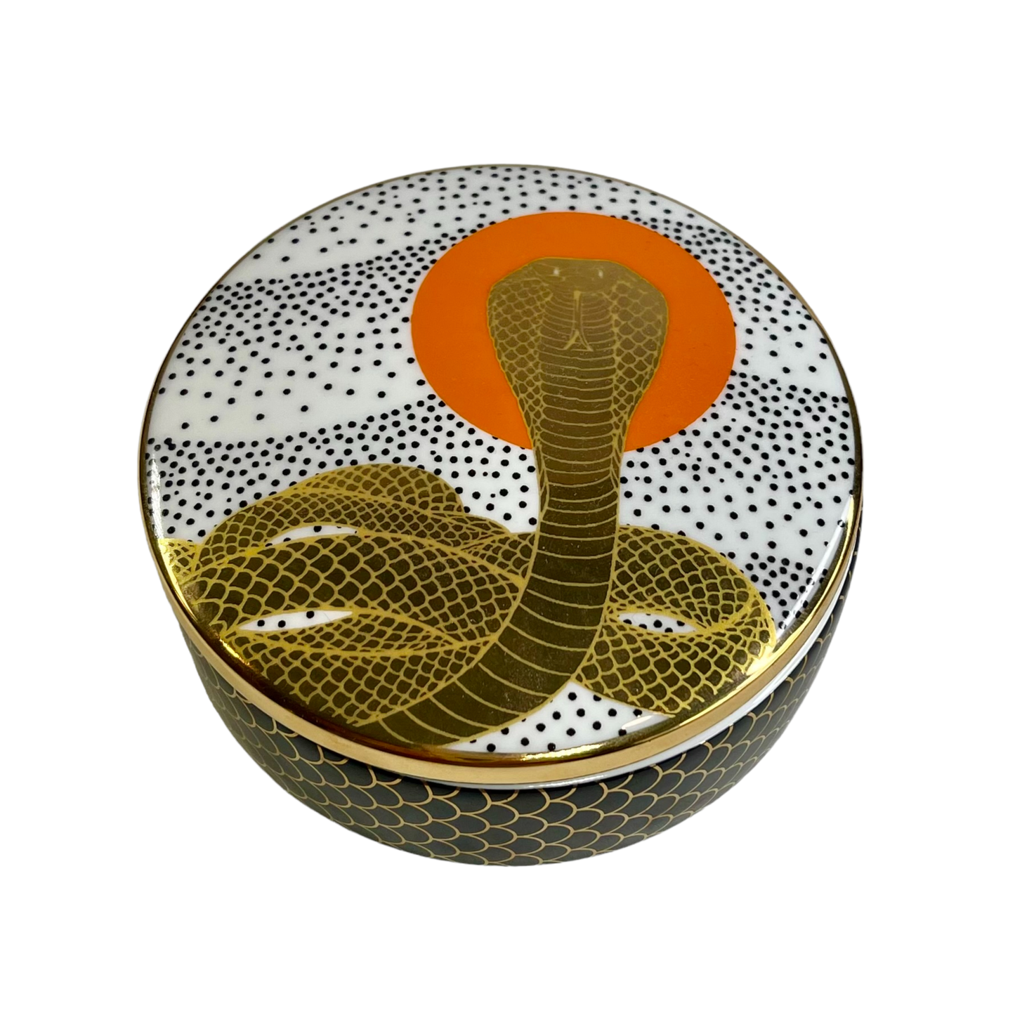 black and white porcelain trinket box with a winding gold cobra in front of an orange circle on a white background
