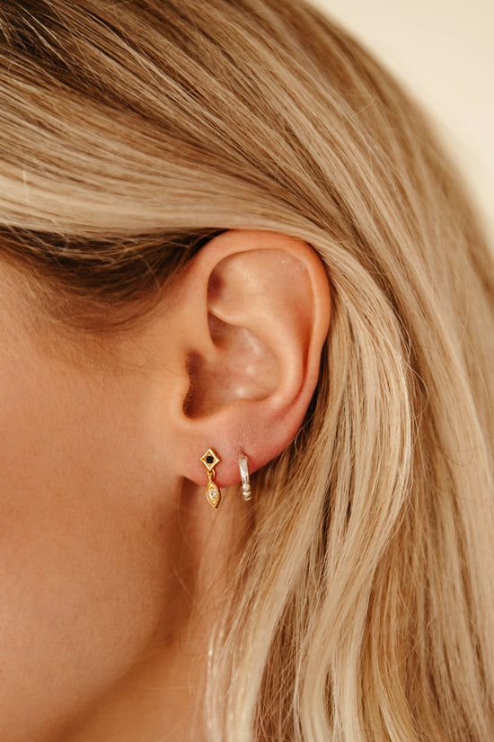 Close-up of an ear wearing a gold earring with a diamond-shaped design.