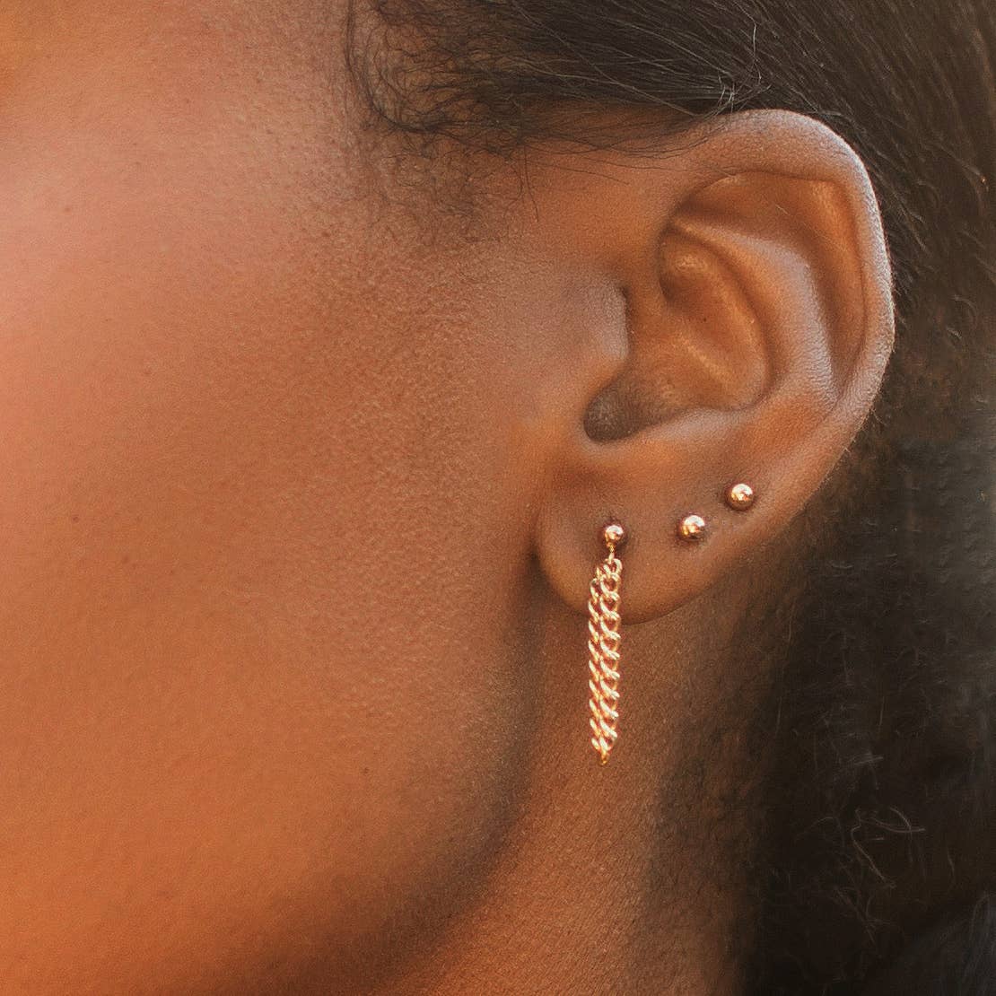 close up of a model wearing the double link drop earrings and two small round gold studs