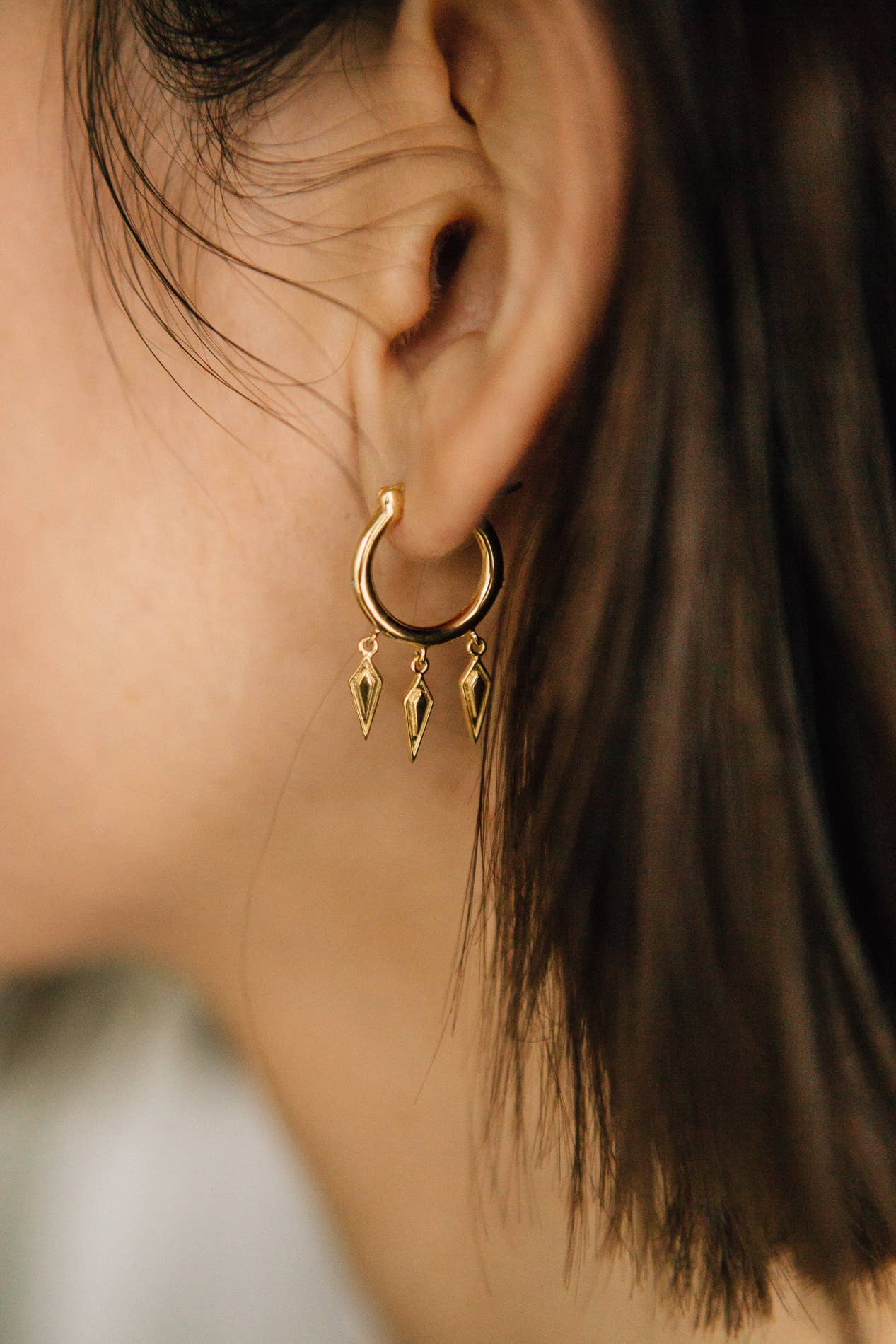 Close-up of a gold hoop earring with dangling charms worn by a person.
