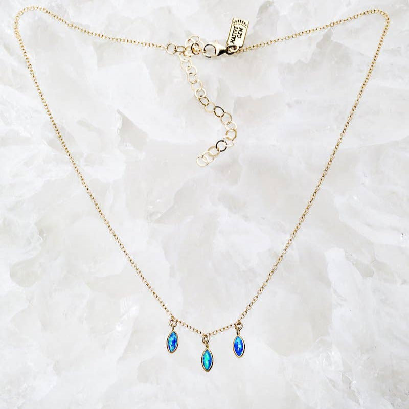 Gold necklace with blue teardrop pendants on a white marble surface