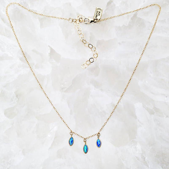 Gold necklace with blue teardrop pendants on a white marble surface