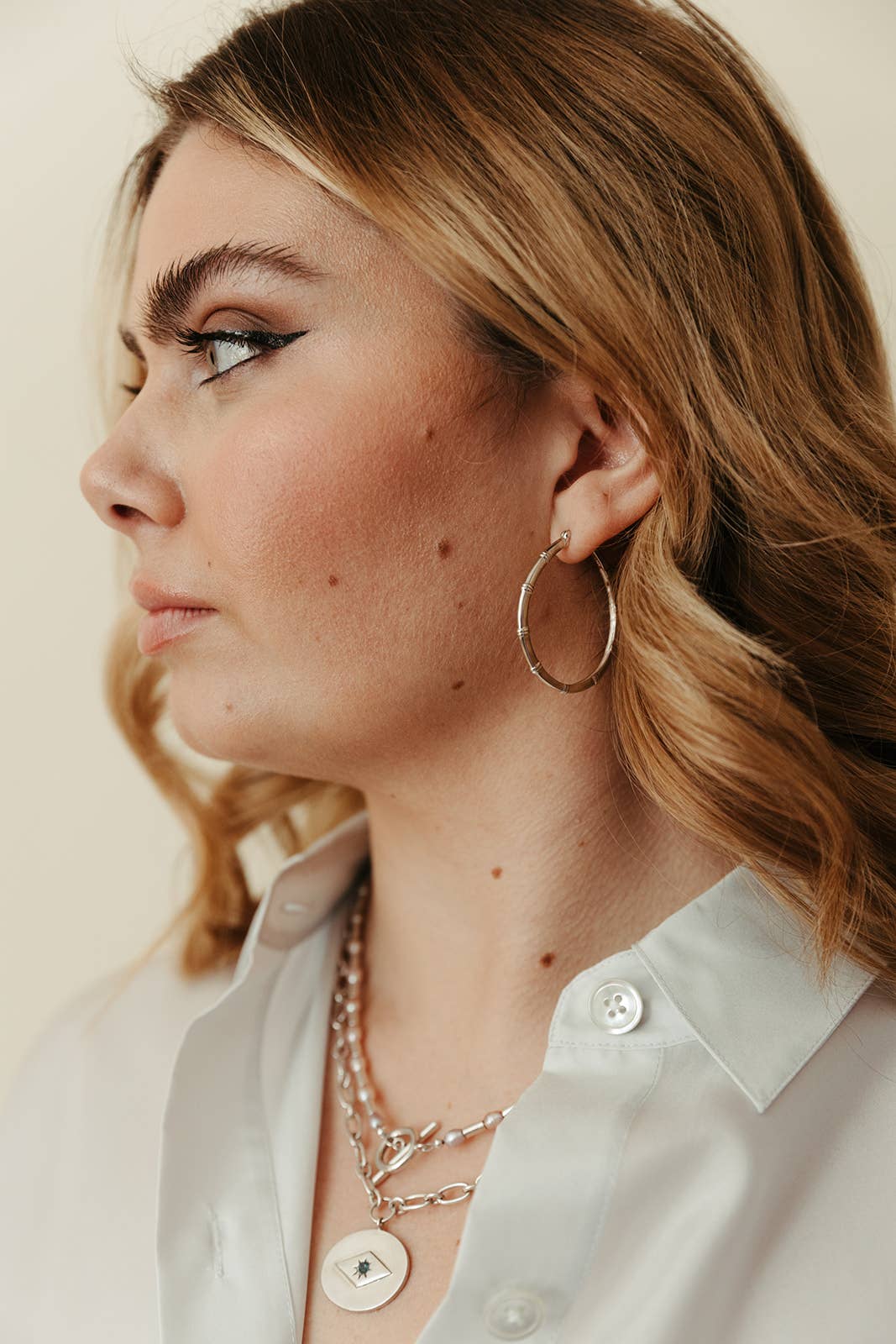 Close-up of a person wearing gold hoop earrings and layered necklaces.