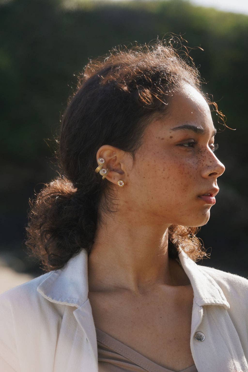 Woman with a neutral expression outdoors, wearing a light-colored jacket.