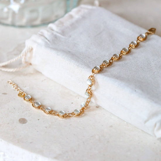 Gold chain bracelet on a white drawstring bag