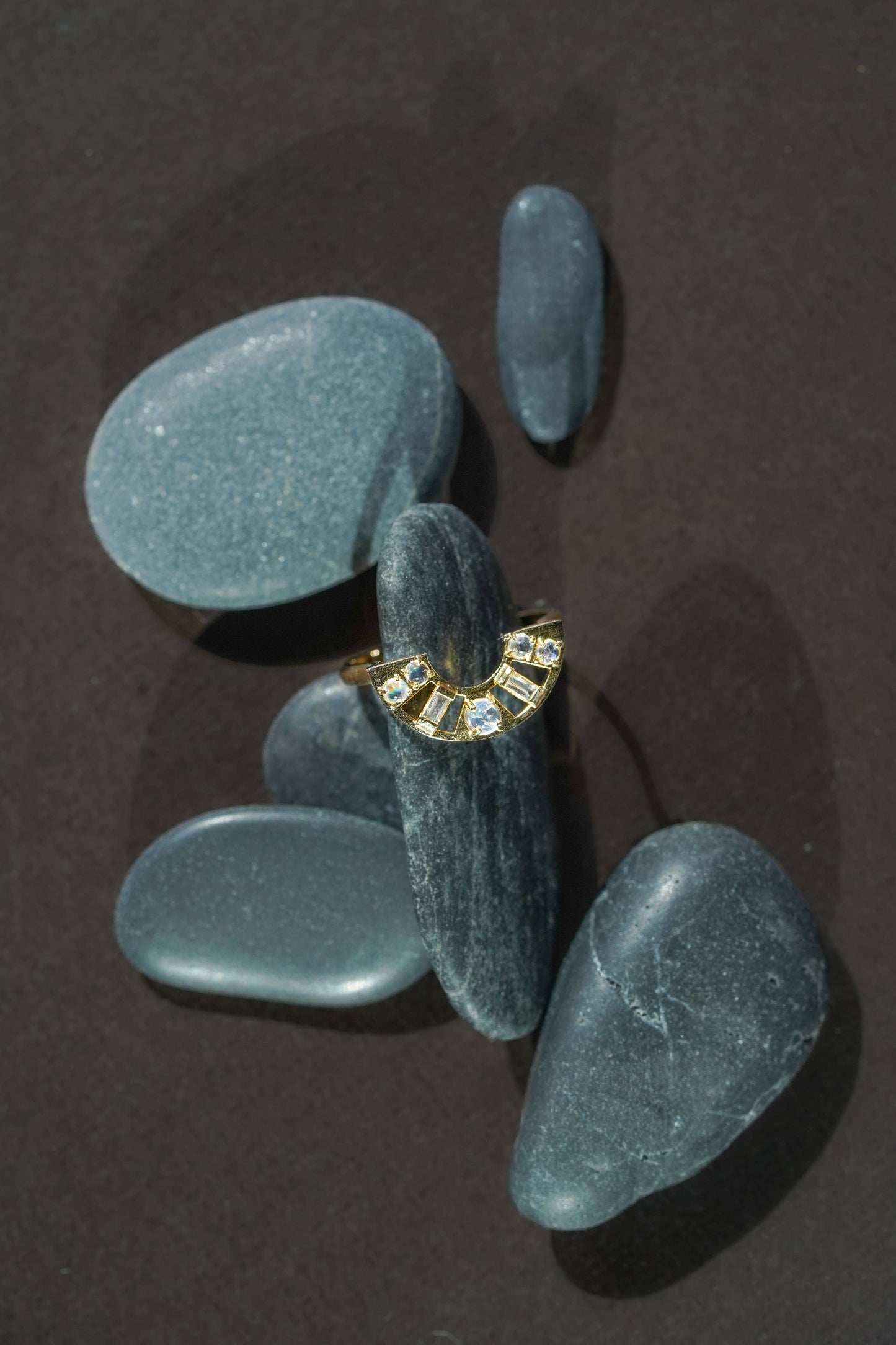 Gold rainbow moonstone and topaz arc ring with gemstones on a dark surface with stones