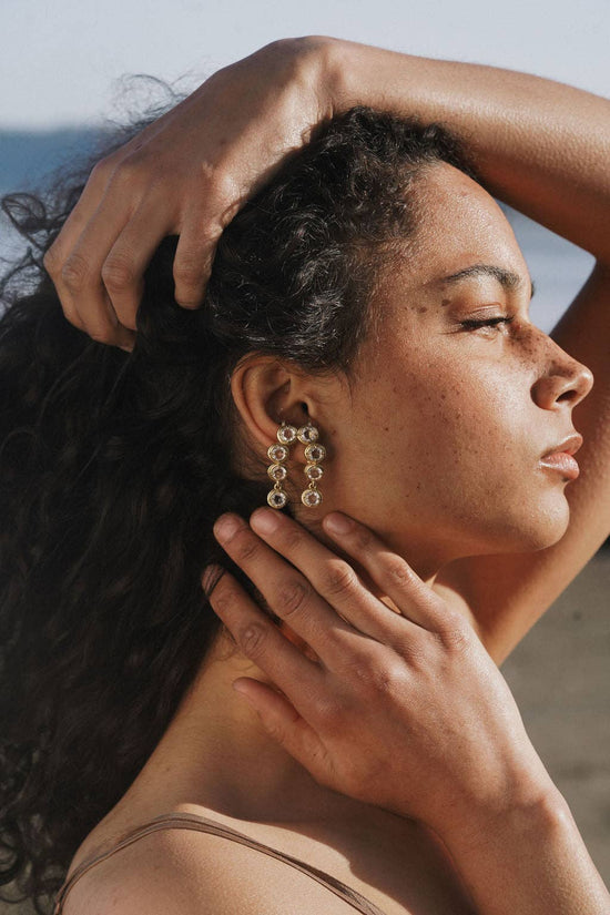 Woman with long dark hair wearing the ear cuff, with a hand adjusting her hair against a blurred natural background