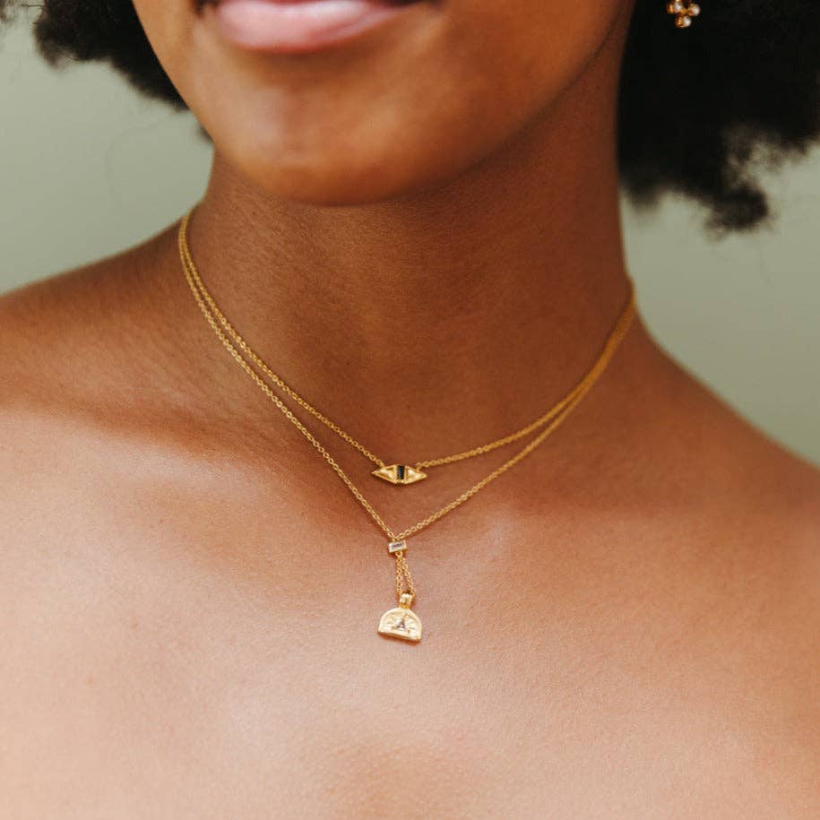 Close-up of a person wearing two gold necklaces with pendants against a neutral background