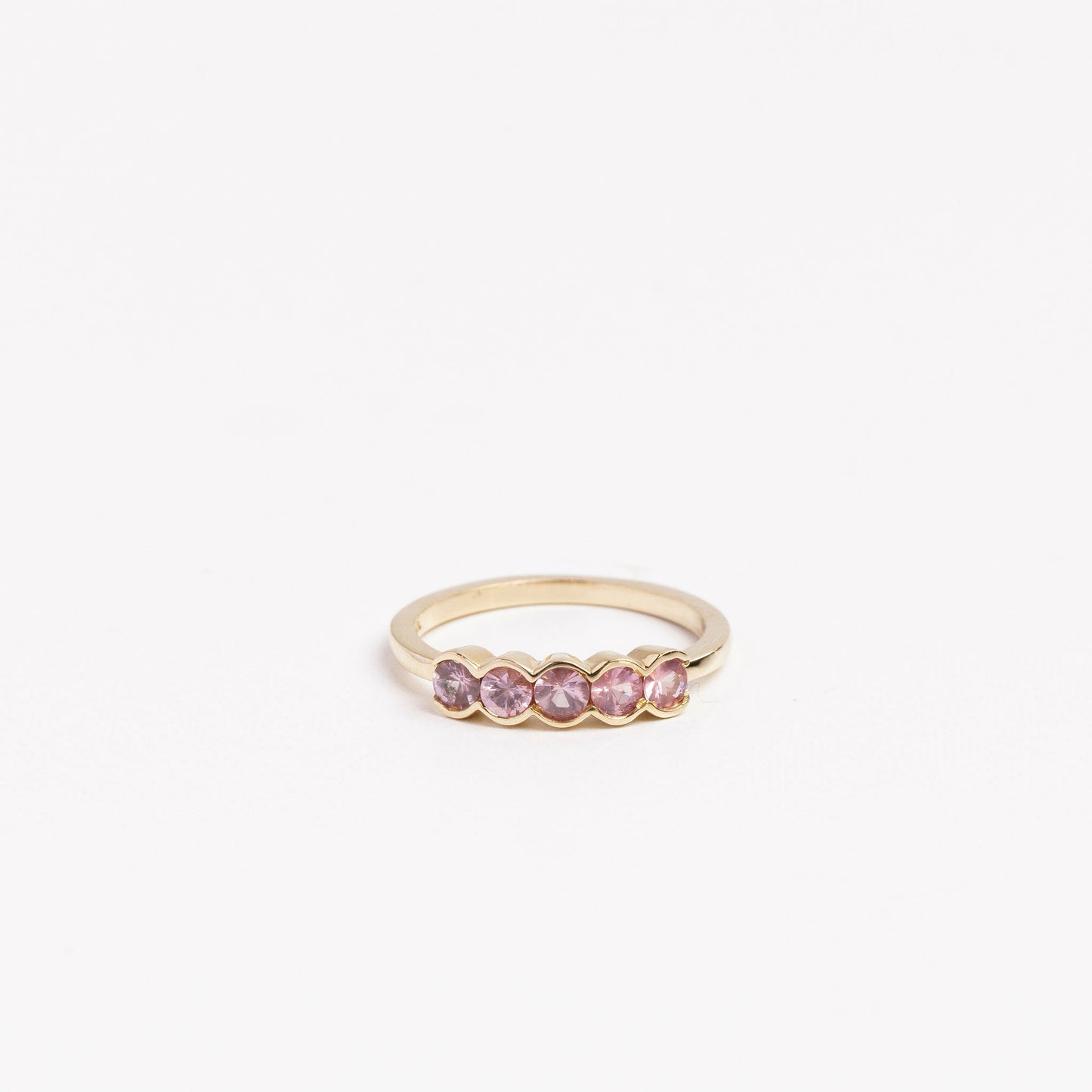 gold ring with 5 pink spinel half bezel set on a white background