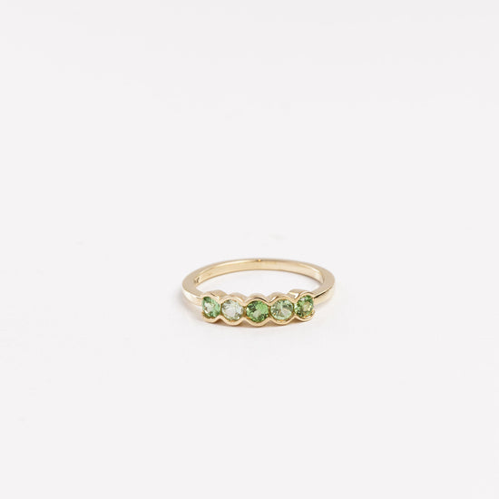 yellow gold ring with 5 half bezel set green garnets on a white background