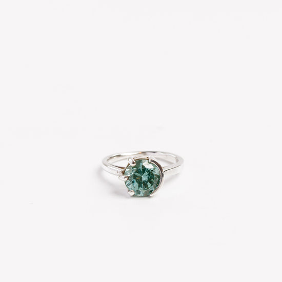 sterling silver ring with green moissanite half bezel half prong set on a white background