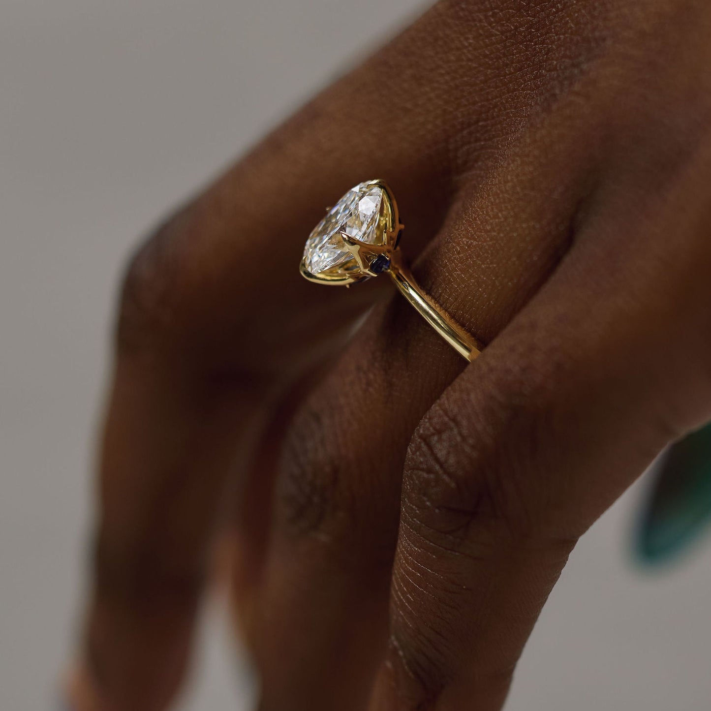 A close-up of a hand wearing a gold ring with a marquise-cut clear gemstone, set against a soft neutral background.