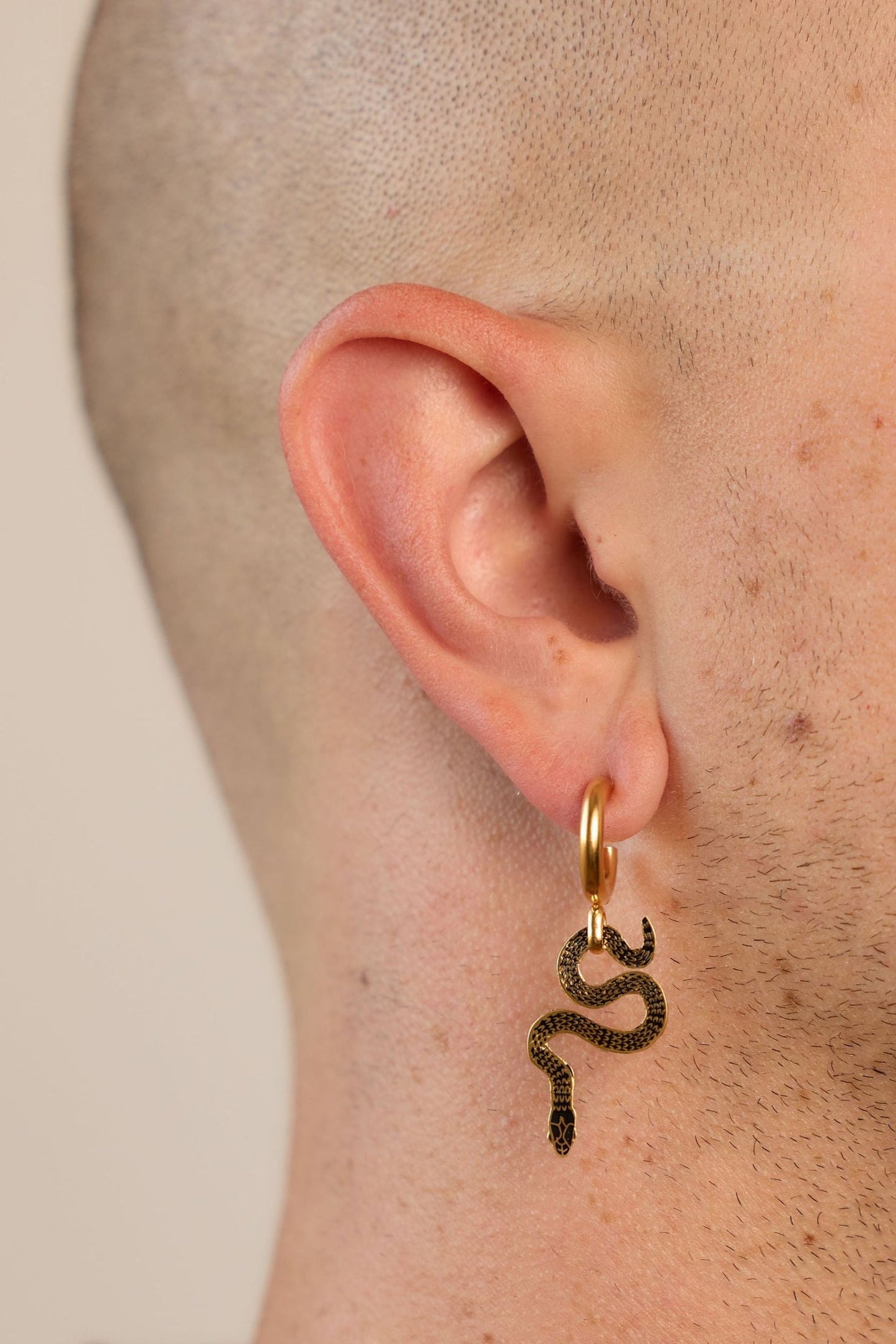 asymmetrical huggie earrings, one with a pear shaped onyx and one with a decorative snake on a model
