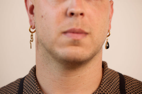 asymmetrical huggie earrings, one with a pear shaped onyx and one with a decorative snake on a model