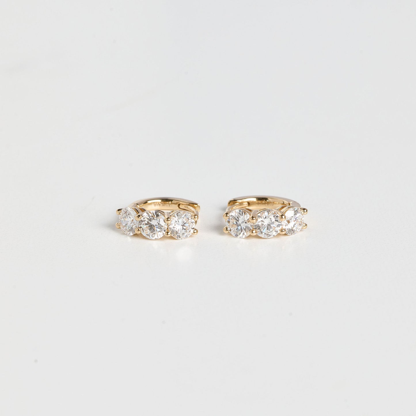 Pair of gold hoop earrings with clear gemstones on a light gray background