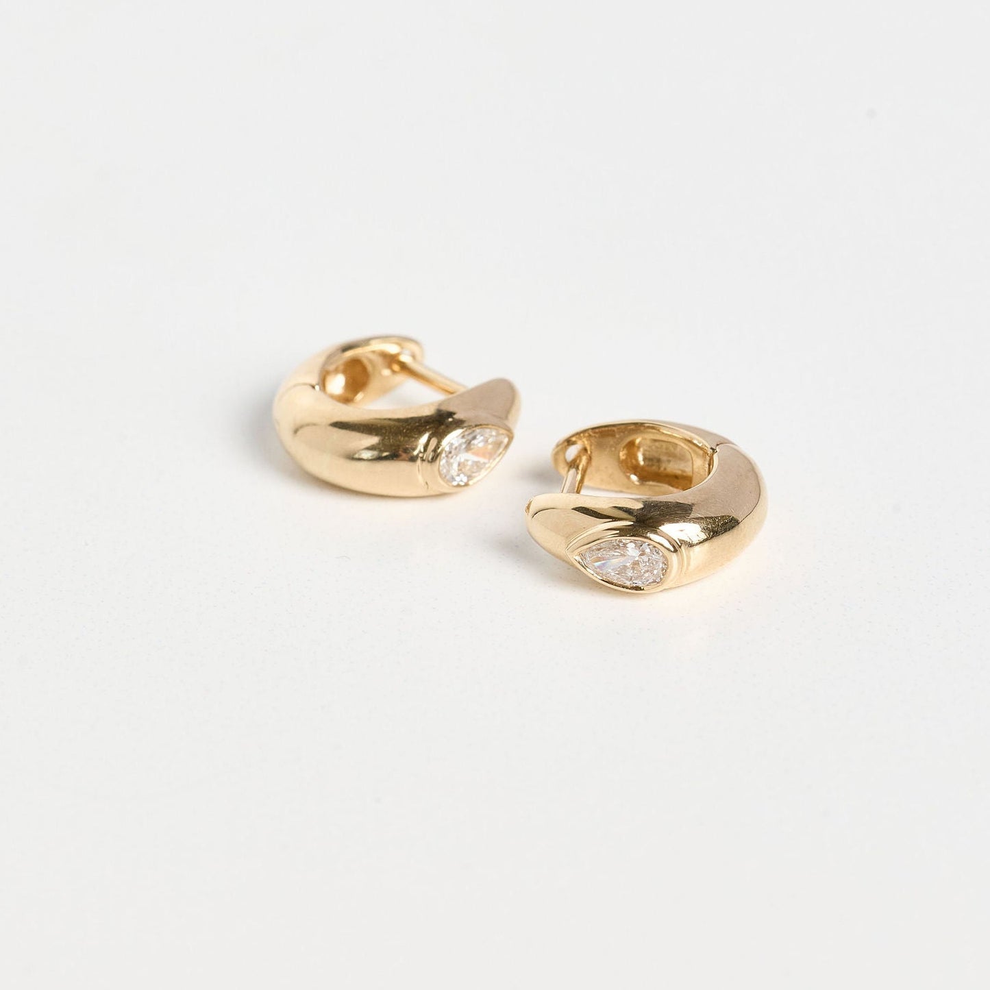 Gold hoop earrings with small stones on a light gray background