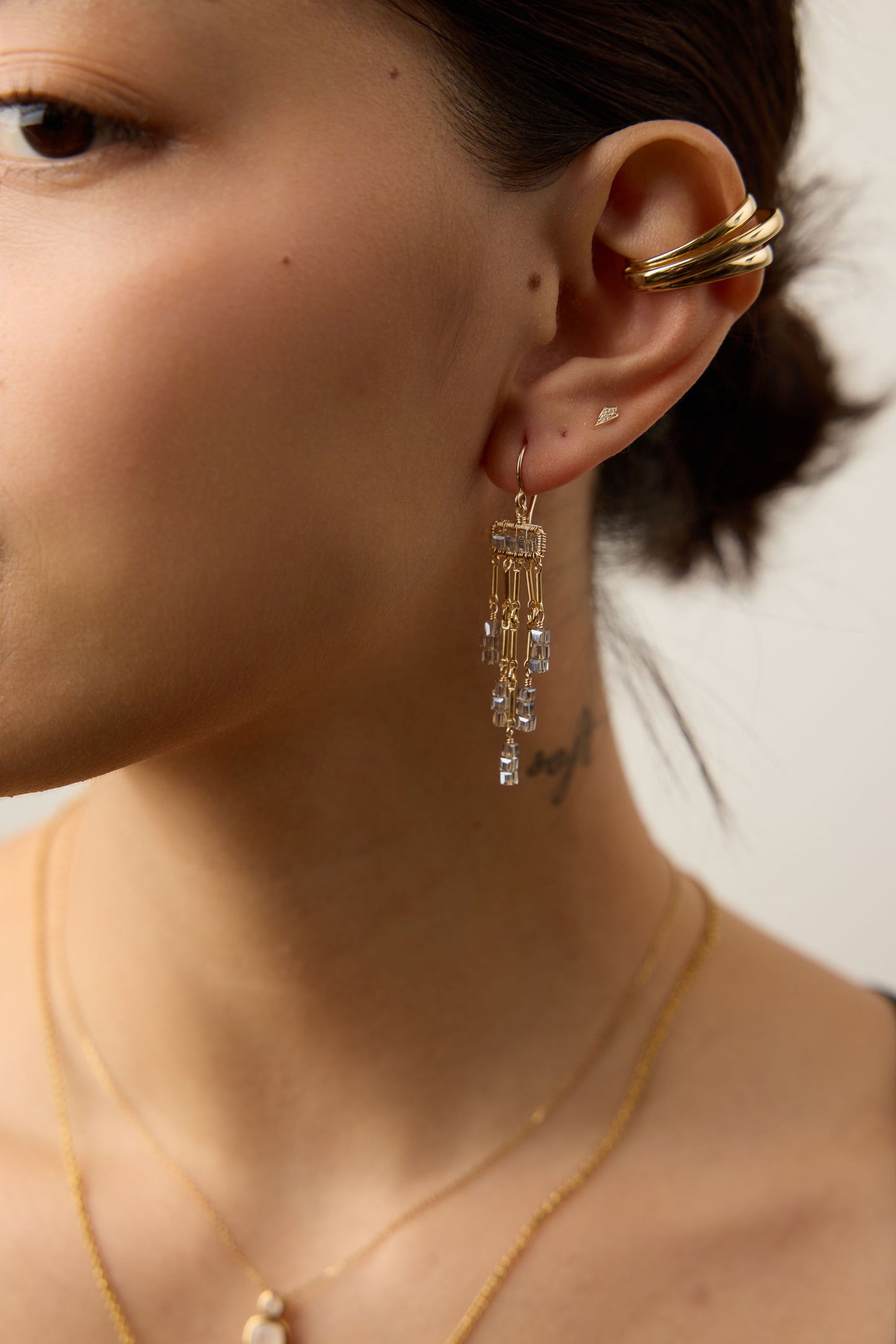 Close-up of a person wearing gold earrings and necklaces against a neutral background
