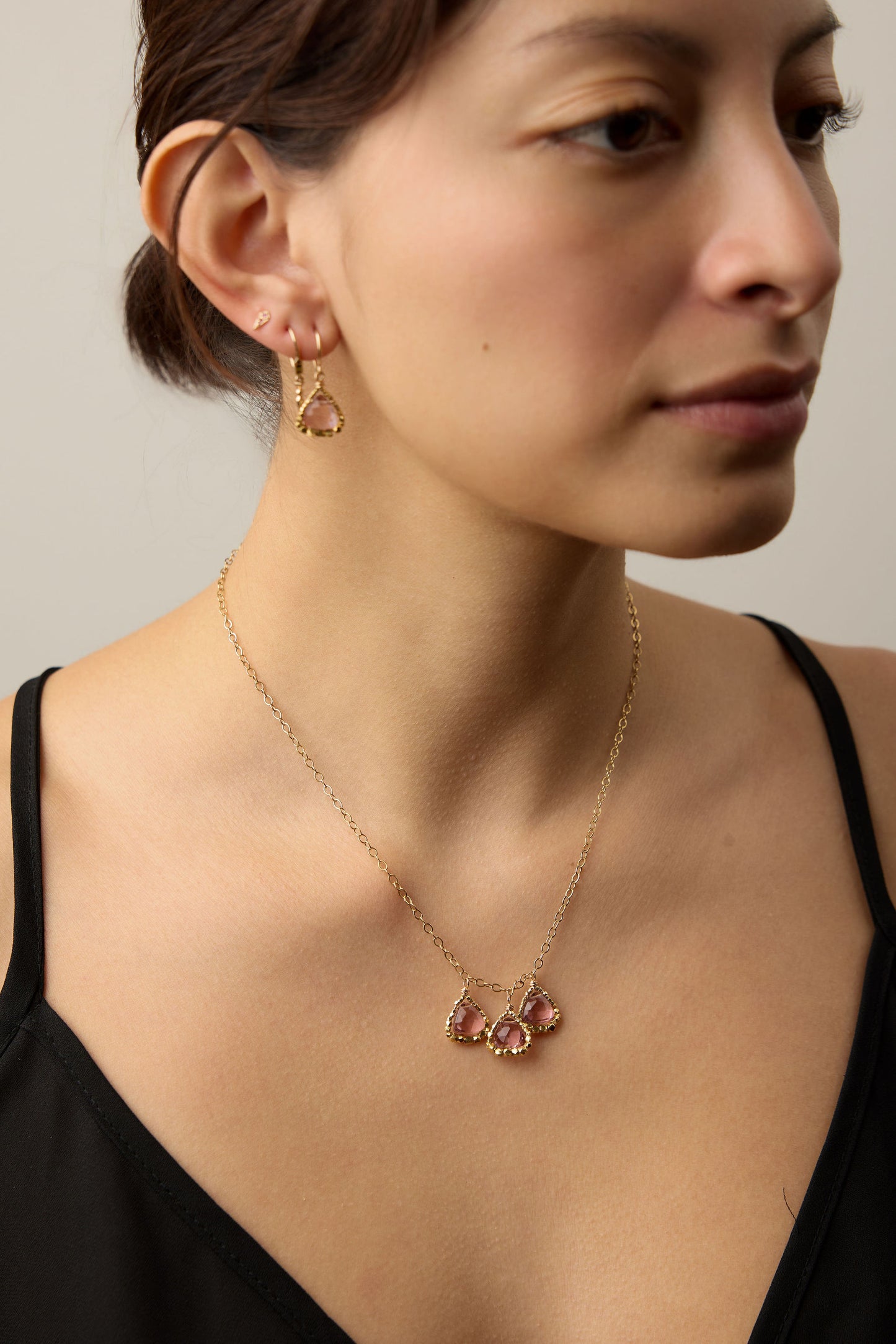 Woman wearing a gold necklace with pink gemstones against a neutral background