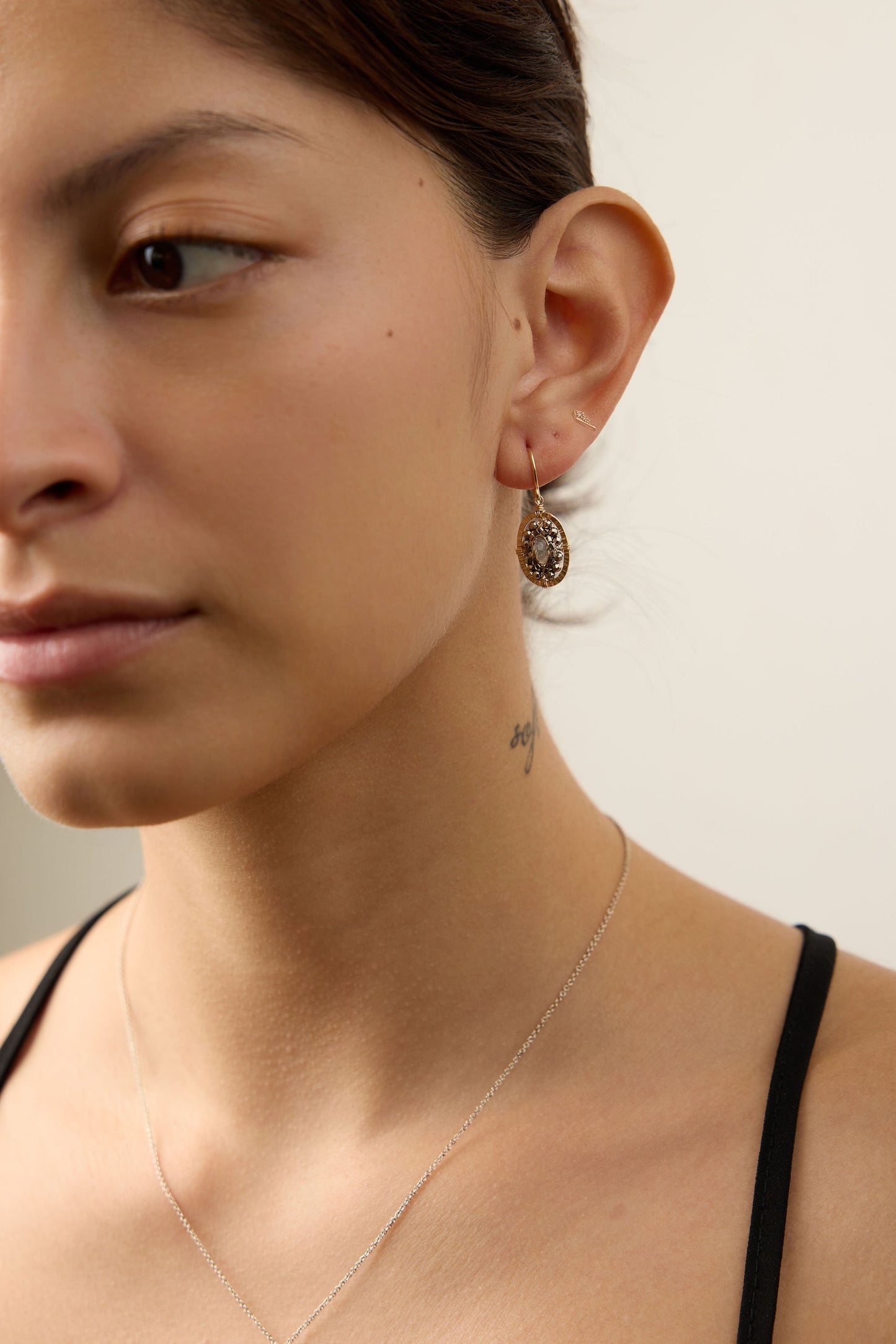 Close-up of a woman wearing a delicate necklace and earrings against a neutral background