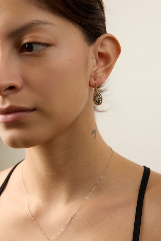 Close-up of a woman wearing a delicate necklace and earrings against a neutral background