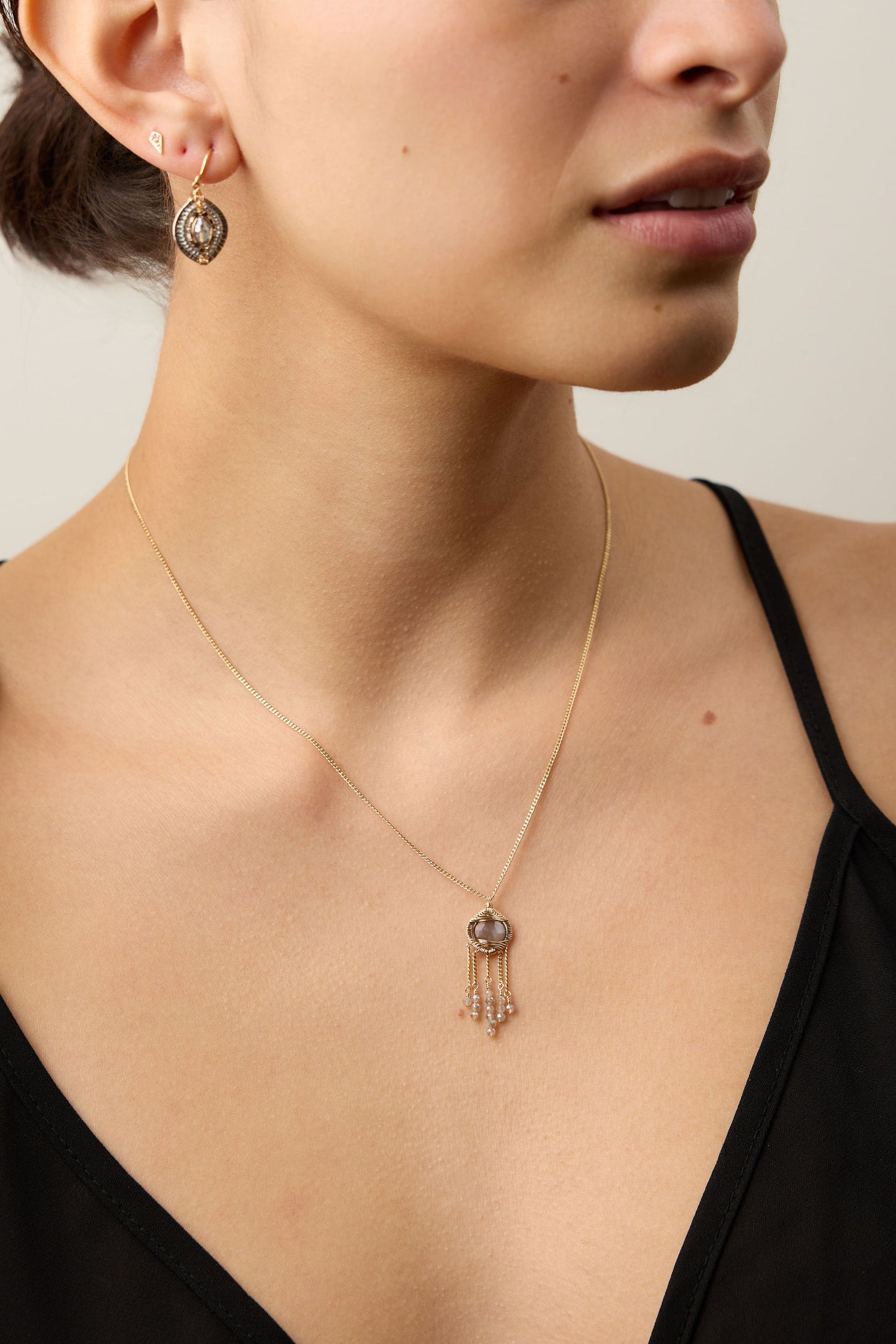 Close-up of a woman wearing a gold necklace with a pendant against a neutral background