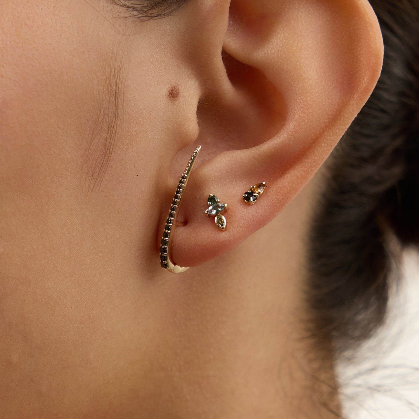Close-up of an ear with multiple earrings against a neutral background