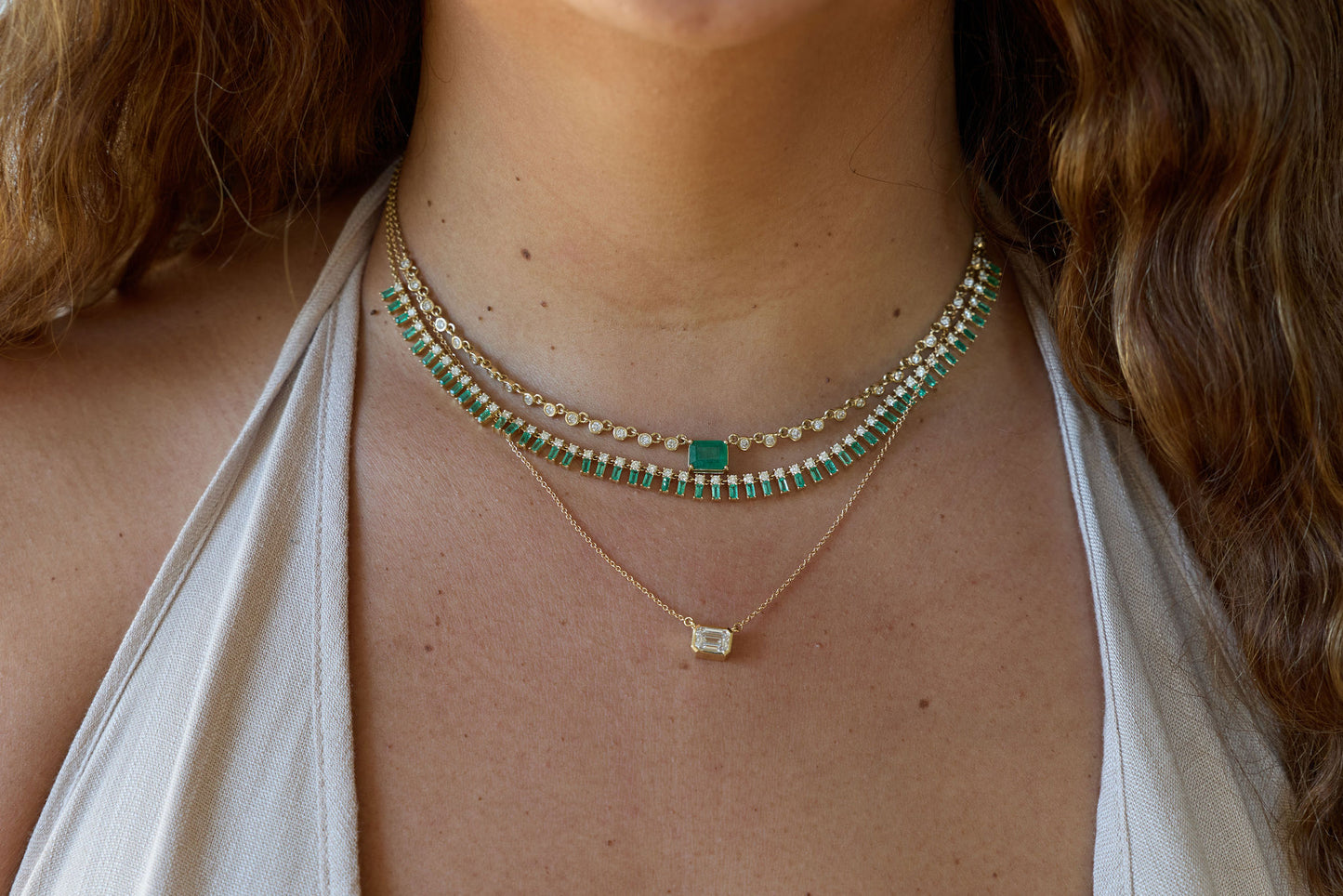 Close-up of a person wearing two necklaces with green gemstones.