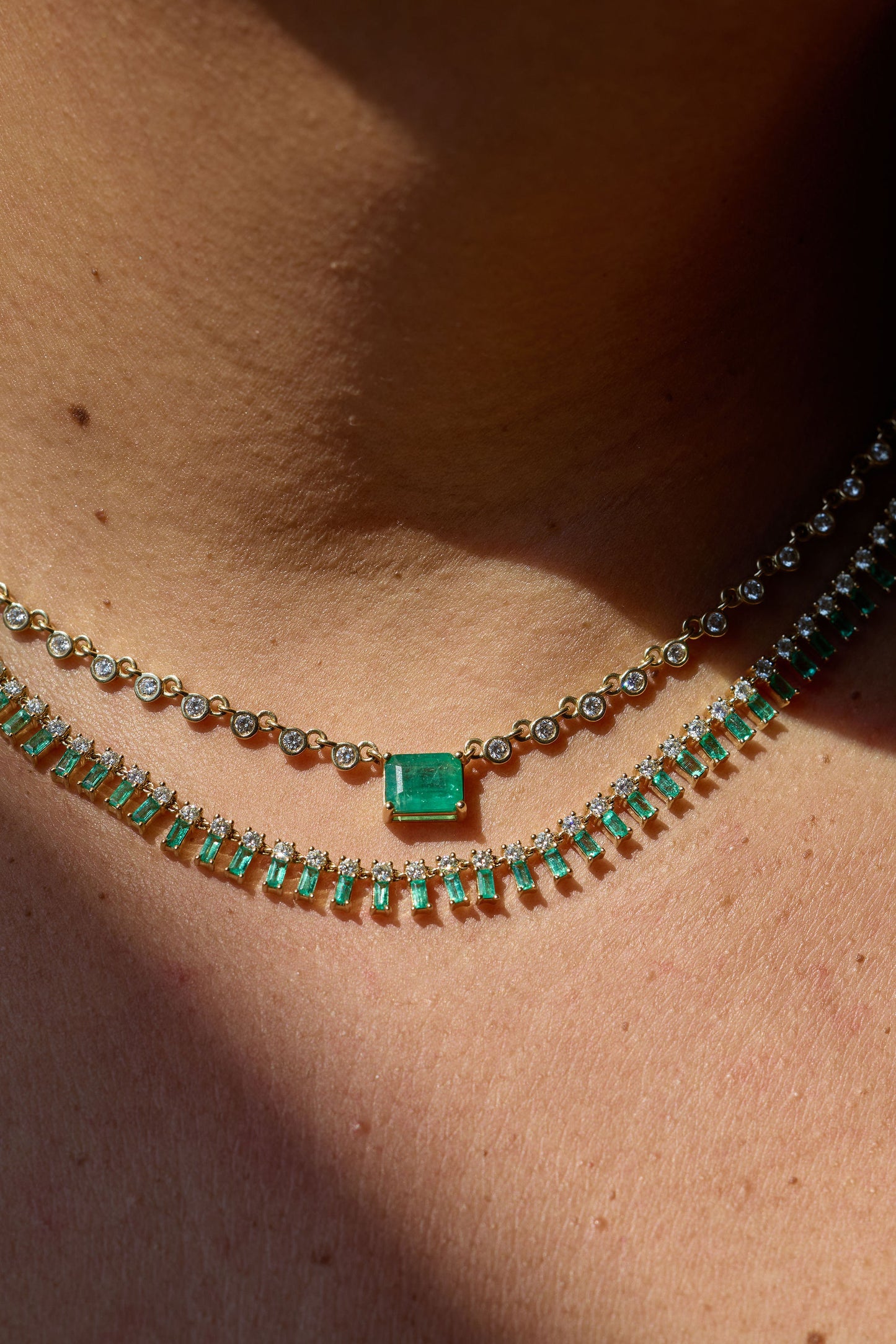 Close-up of a person wearing two emerald necklaces on a light skin background