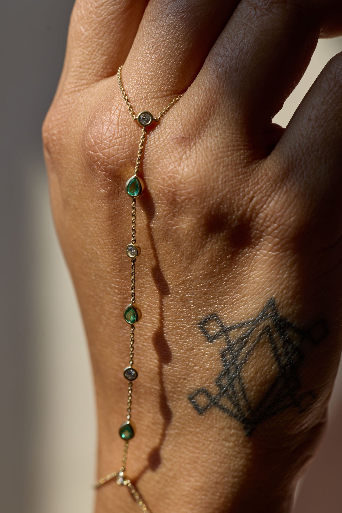 Close up of hand modeling a gold hand chain with emeralds and diamonds