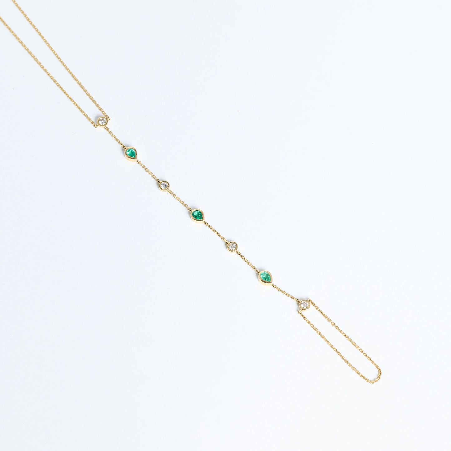 Gold hand chain with emeralds and diamonds close up on white background
