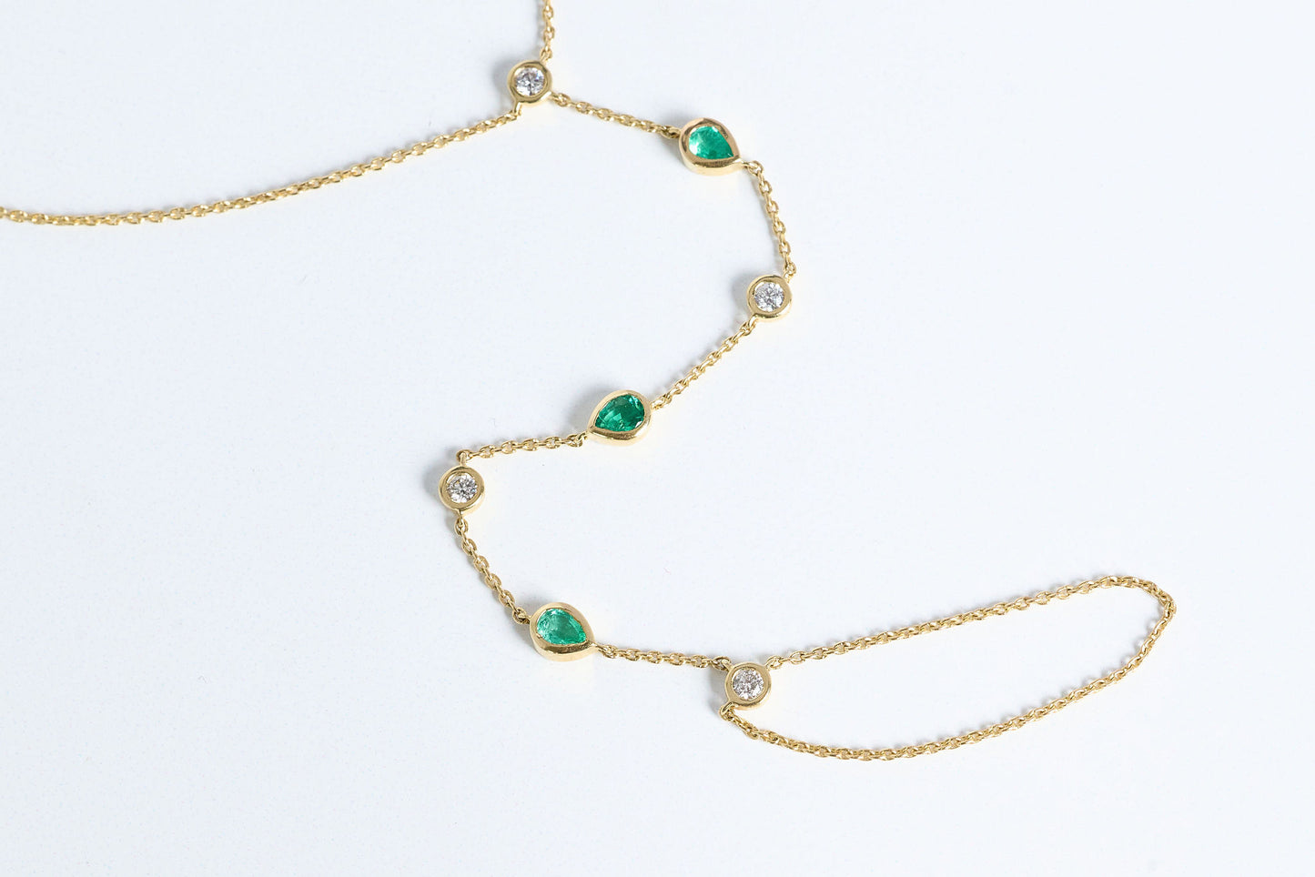 Gold hand chain with emeralds and diamonds close up on white background
