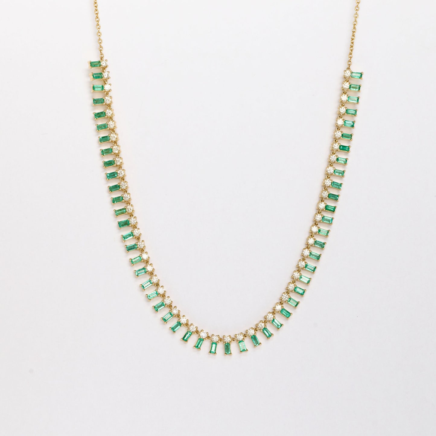 Gold necklace with white diamonds and emerald gemstones on a white background