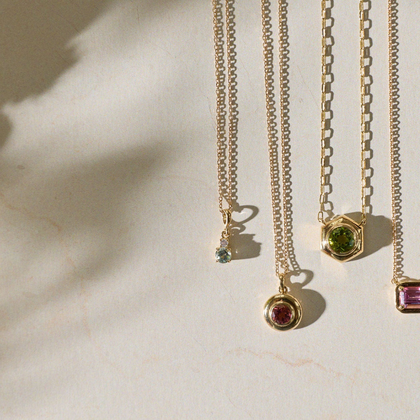 Gold necklaces with gemstone pendants on a light background