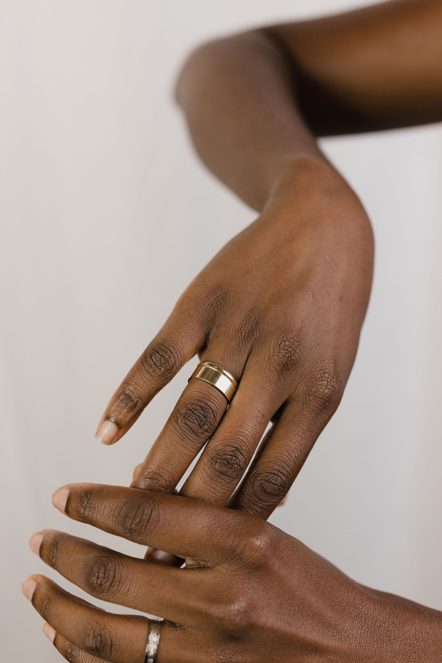 model wearing a wide flat wedding band stacked with a smaller gold band on their ring finger