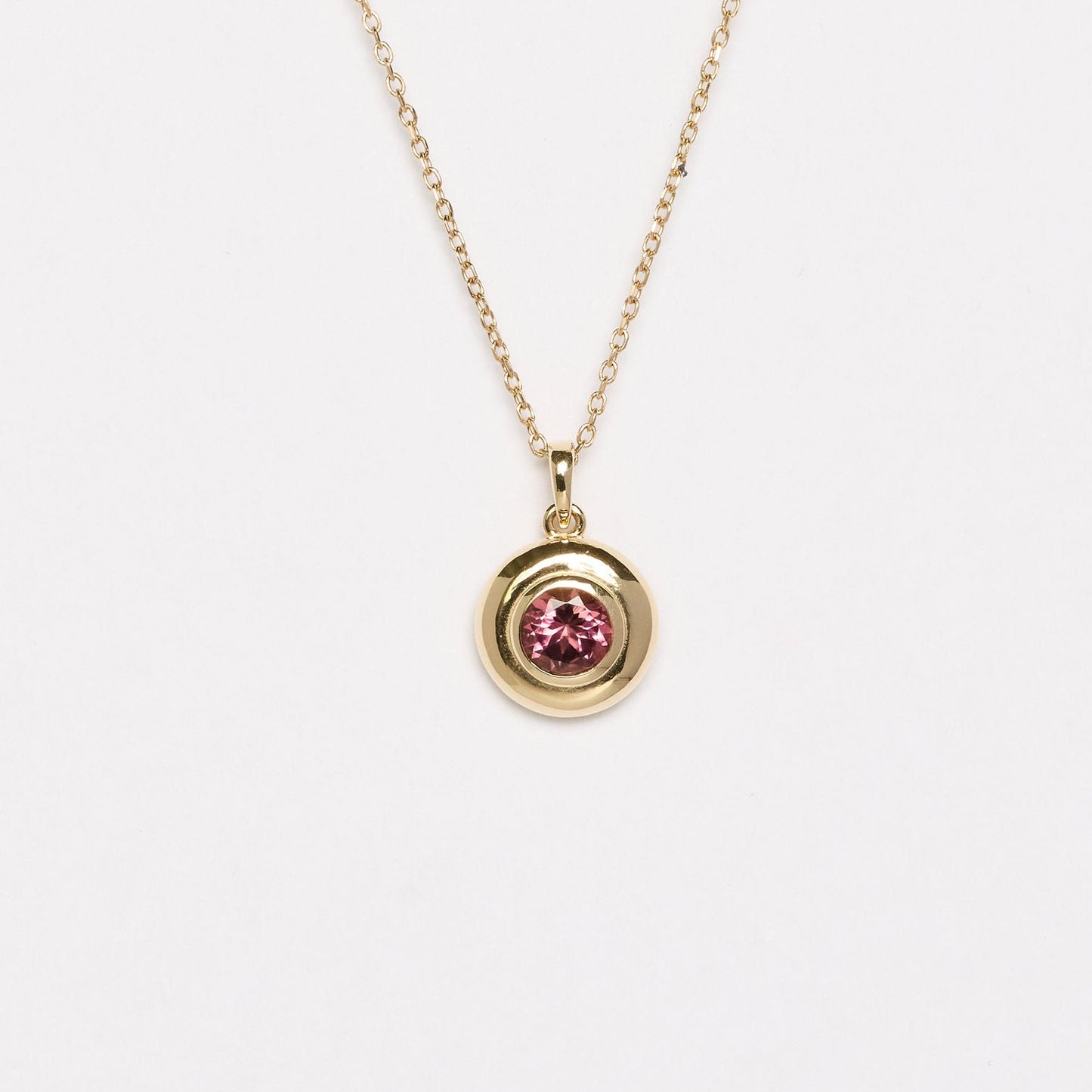 Gold necklace with a pink gemstone pendant on a white background