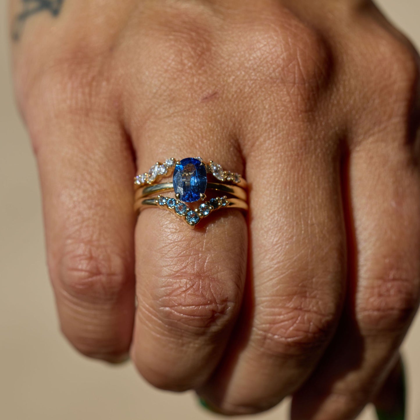 Hand wearing two rings with a blue gemstone on a neutral background