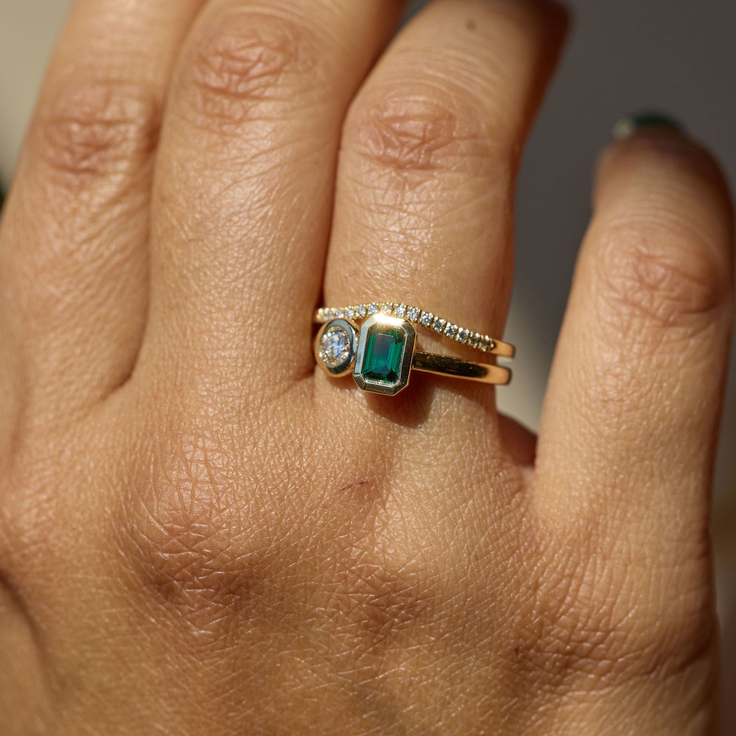 Close-up of a hand wearing a gold ring with a green gemstone on a neutral background