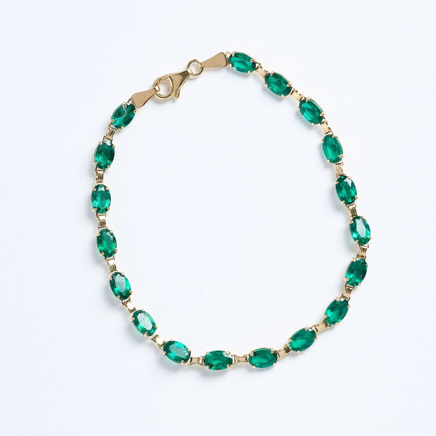 Gold bracelet with green gemstones on a light gray background