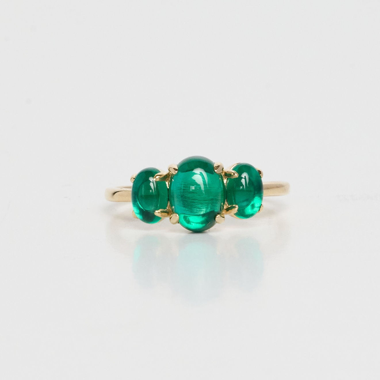 Gold ring with three green gemstones on a light gray background