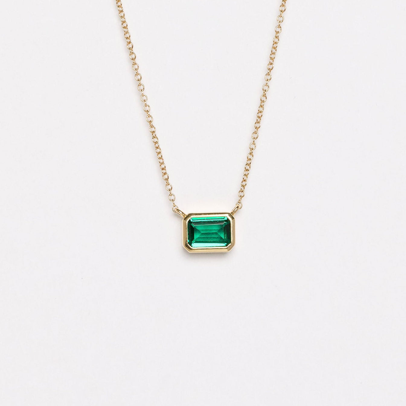 Gold necklace with a green gemstone pendant on a light gray background