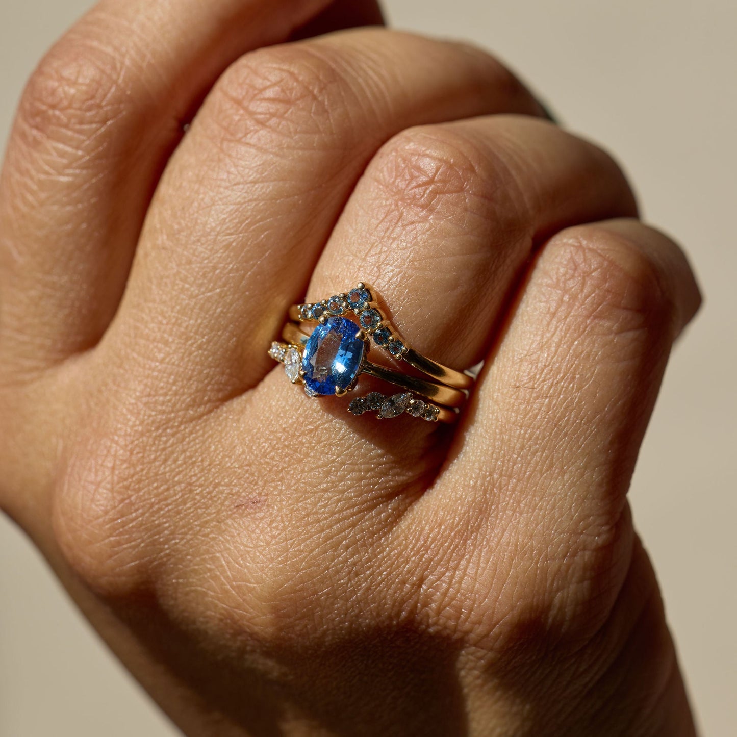 Hand wearing a ring with a blue gemstone on a neutral background
