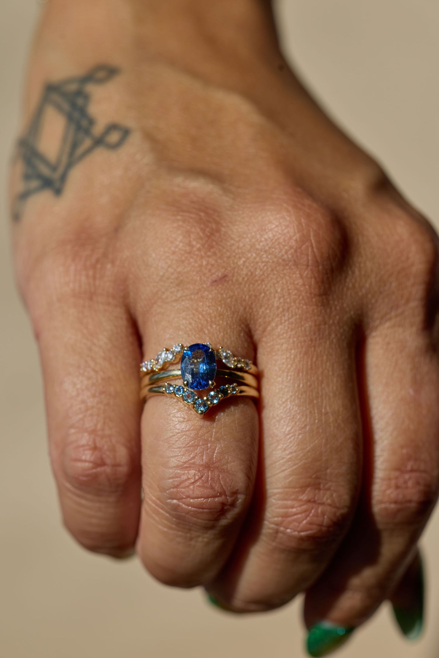 Hand wearing two rings with a blue gemstone on a neutral background