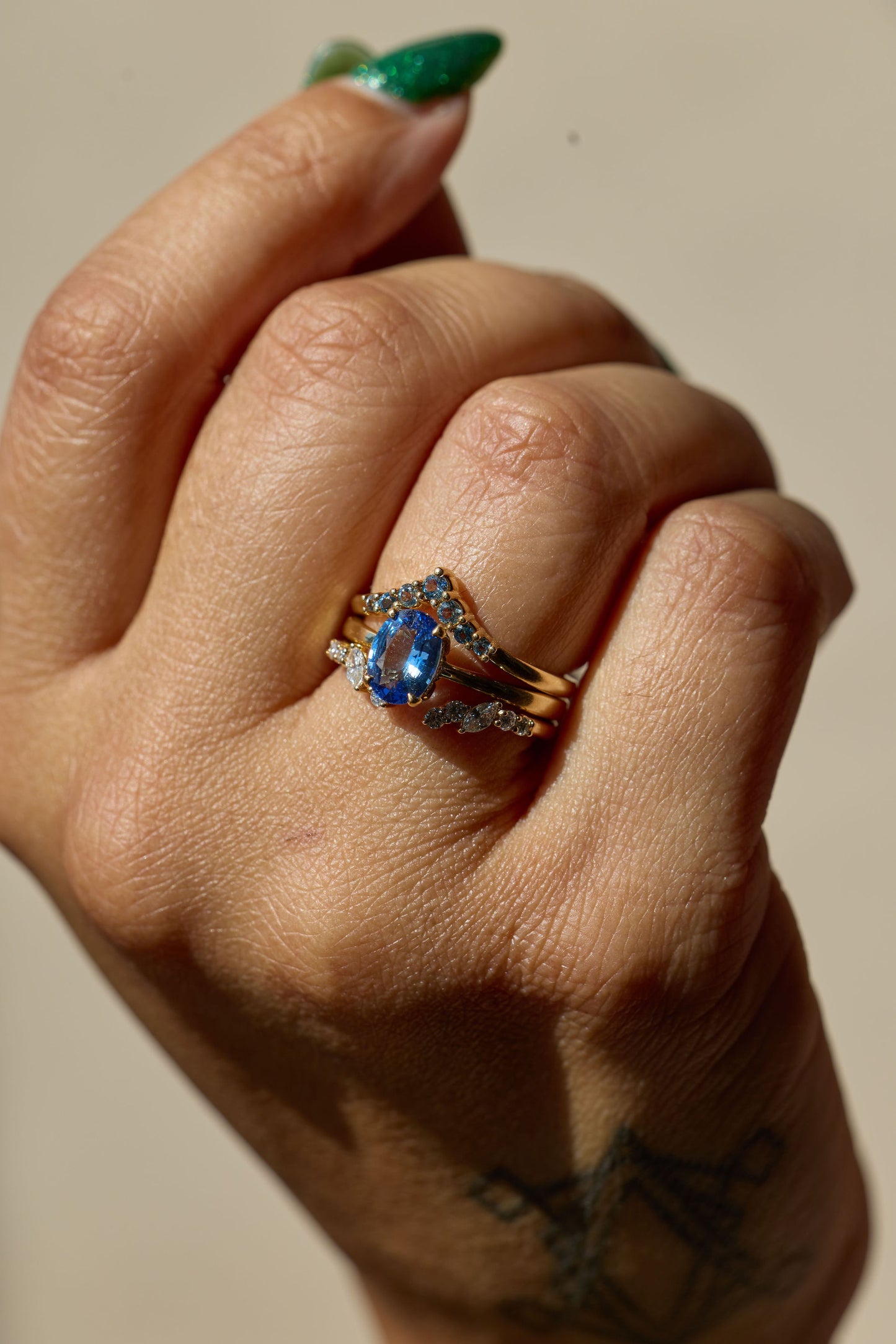 Hand wearing a ring with a blue gemstone on a neutral background