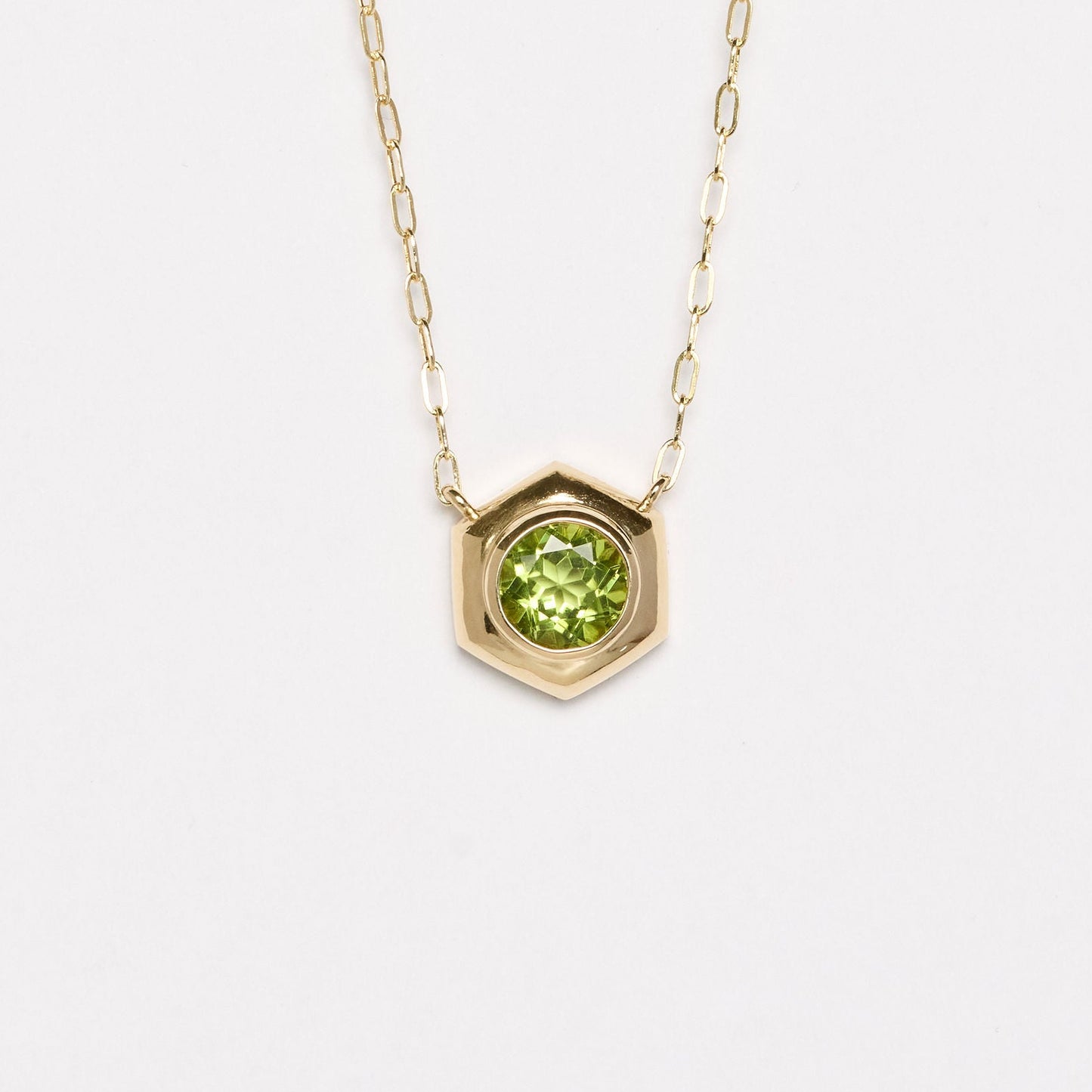 Gold necklace with a green gemstone pendant on a white background