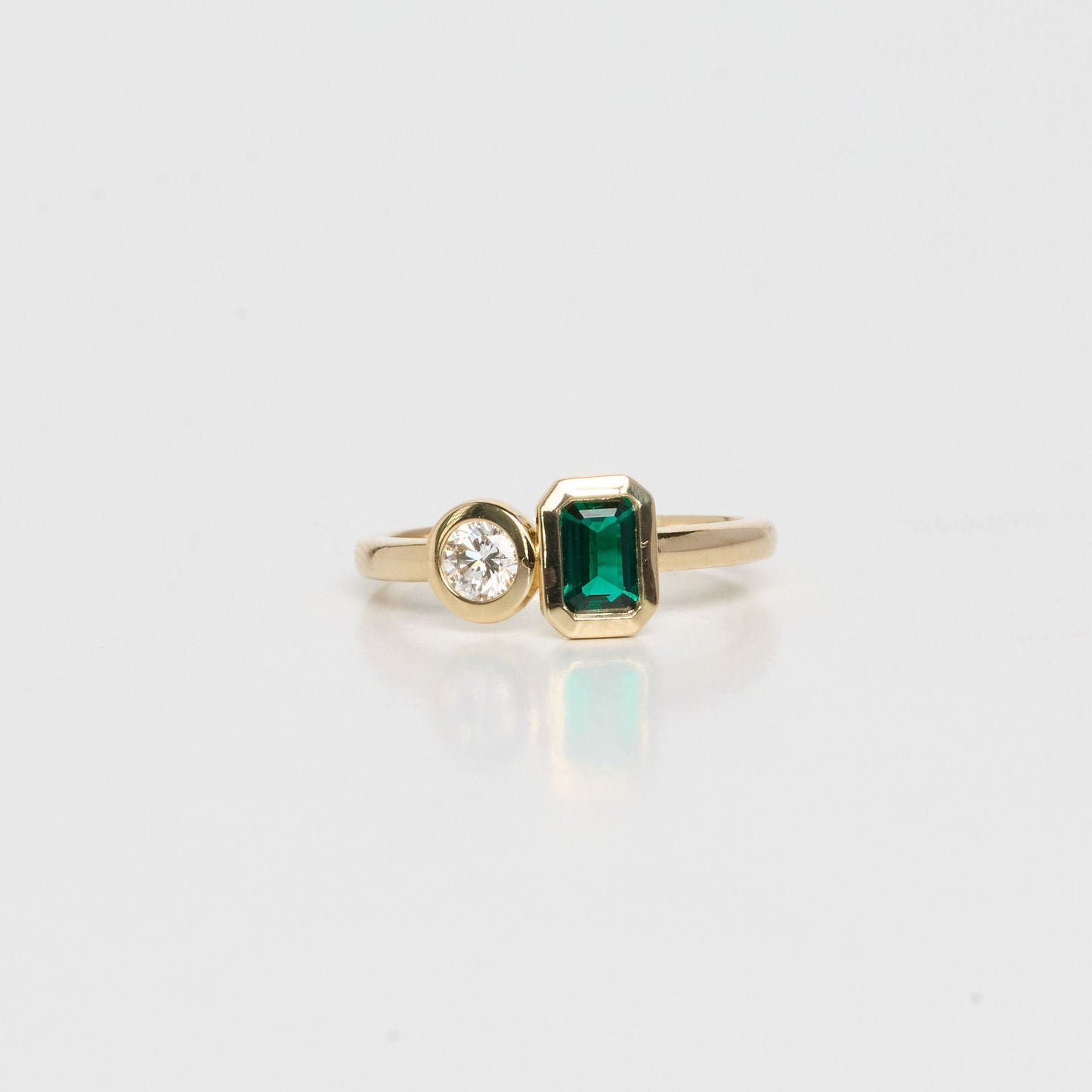 Gold ring with a green gemstone and diamond on a light gray background