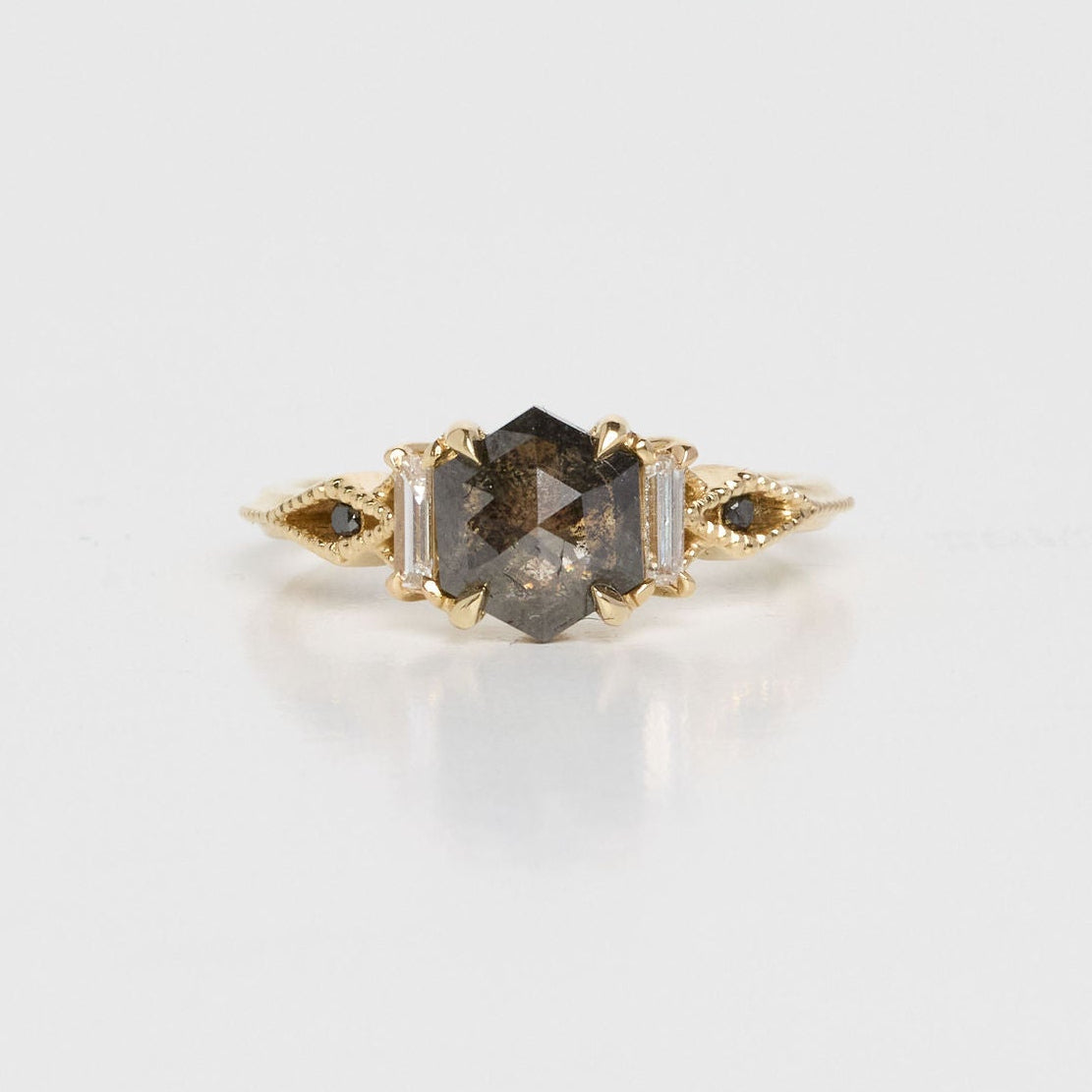 Gold ring with a central dark gemstone on a light gray background