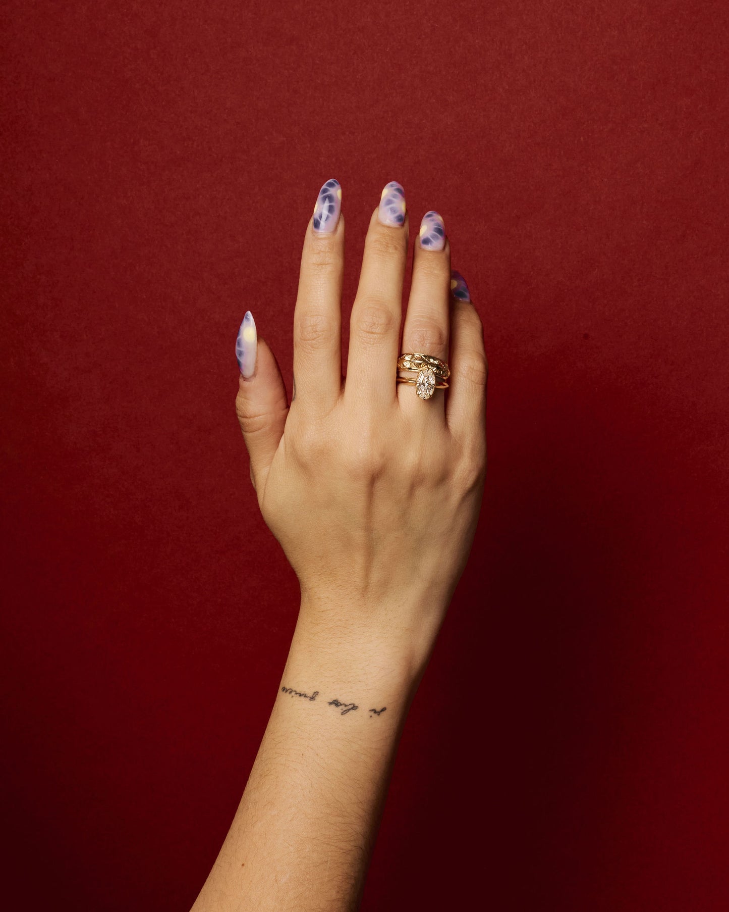 hand wearing the element 2 ring on ring finger stacked with an engraved gold band on red background